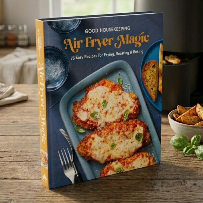 Good Housekeeping Air Fryer Magic cookbook on a wooden table with food in the background