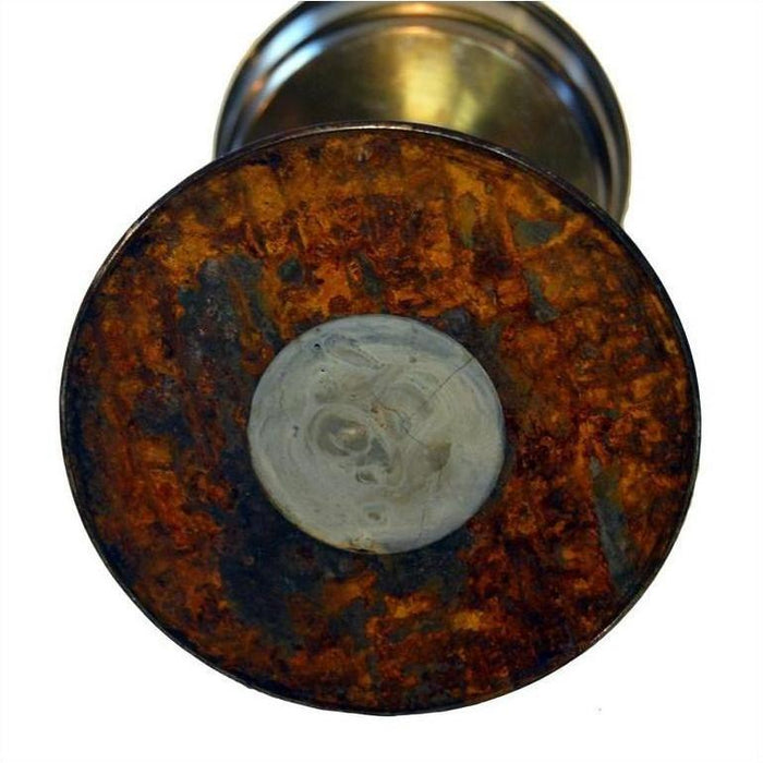 Close-up of rusted brass base of antique oil lamp with circular gray patch in center.