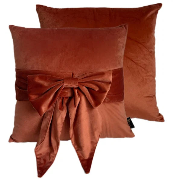 Two rust-colored pillows with velvet bows on a white background