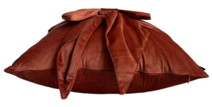 A brown velvet throw pillow with a large bow on top, shown against a plain white background.