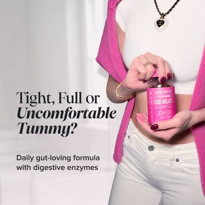A woman in a white crop top, pink cardigan, and white jeans holds a bottle of Novomins De-Blo Gummies. The image features promotional text on the left reading 'Tight, Full or Uncomfortable Tummy?' and 'Daily gut-loving formula with digestive enzymes'.