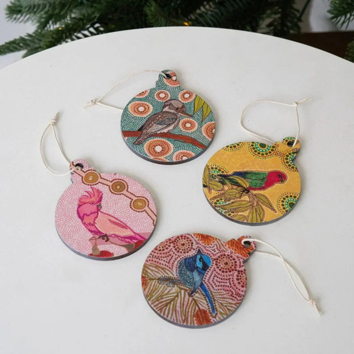 Four colorful bird-themed Christmas ornaments on a white surface with a blurred green background.