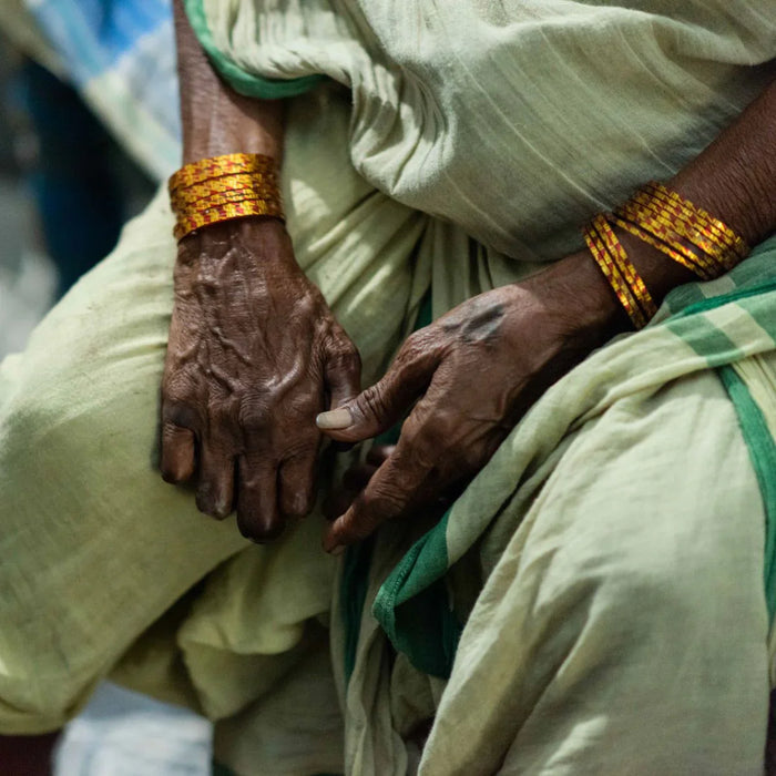 Close-up of two hands with gold bracelets on a person wearing a light green garment.