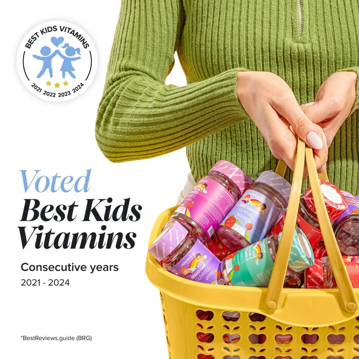 A woman in a green jumper carries a yellow shopping basket filled with Novomins gummy bottles, beside a Best Kids Vitamins badge and the heading 'Voted Best Kids Vitamins, consecutive years 2021 to 2024', credited to BestReviews.guide.