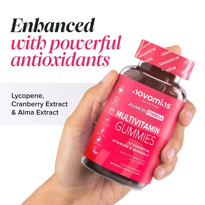 A hand holding a bottle of Novomins Multivitamin Gummies with the cap off, headed 'Enhanced with powerful antioxidants' listing lycopene, cranberry extract and amla extract. The label reads 17 essential vitamins and minerals with vitamins A, B6, B12, C and zinc, 60 peach flavoured gummies.