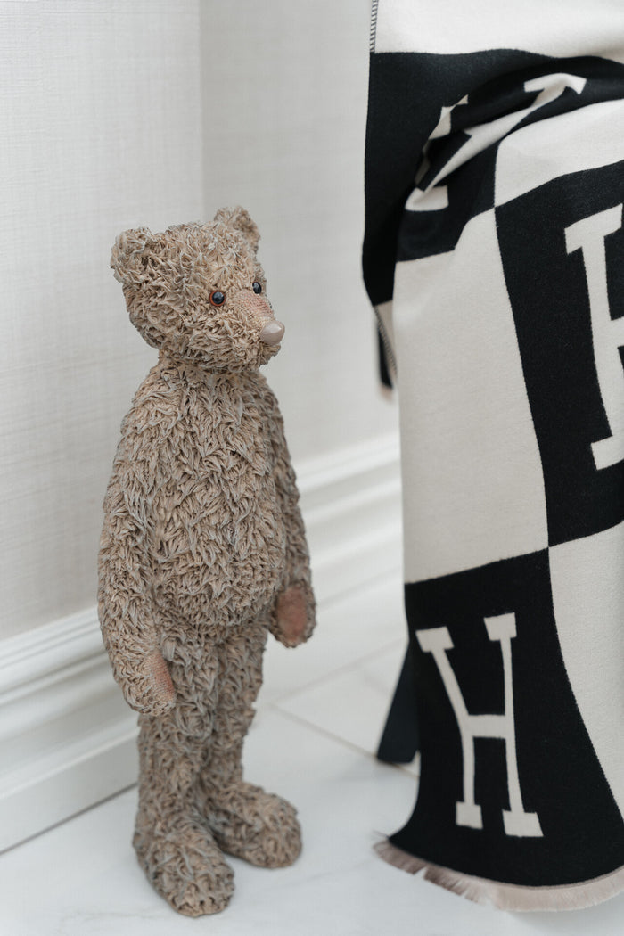 Teddy bear standing next to a black and white patterned fabric with 'H' logo.
