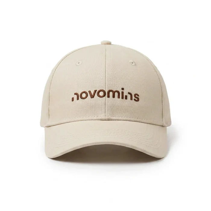 Front view of a cream Novomins baseball cap on a white background, with the novomins wordmark embroidered in brown across the front panel.