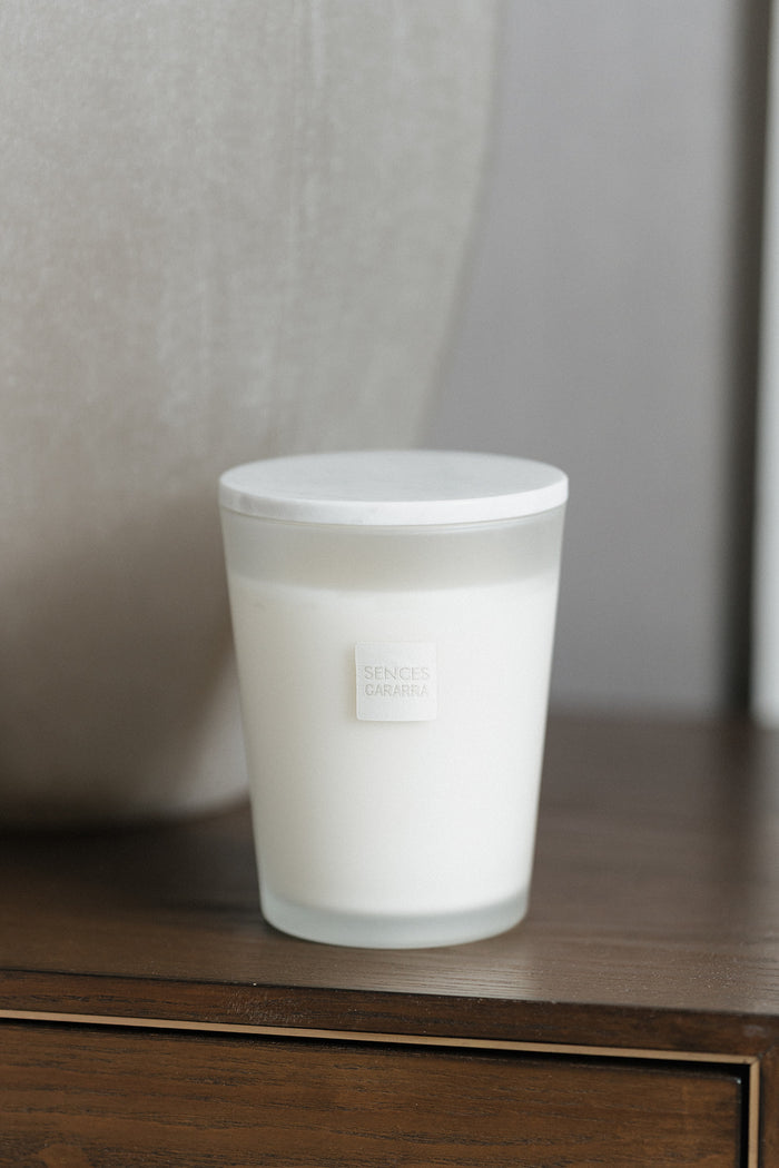 A frosted glass jar candle with a white lid and a small square label reading 'Scented Ceramics' sits on a dark wooden surface against a soft gray background.