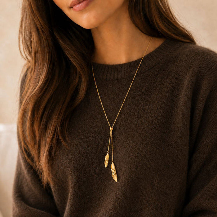 Woman wearing a gold necklace with leaf pendants on a brown sweater.