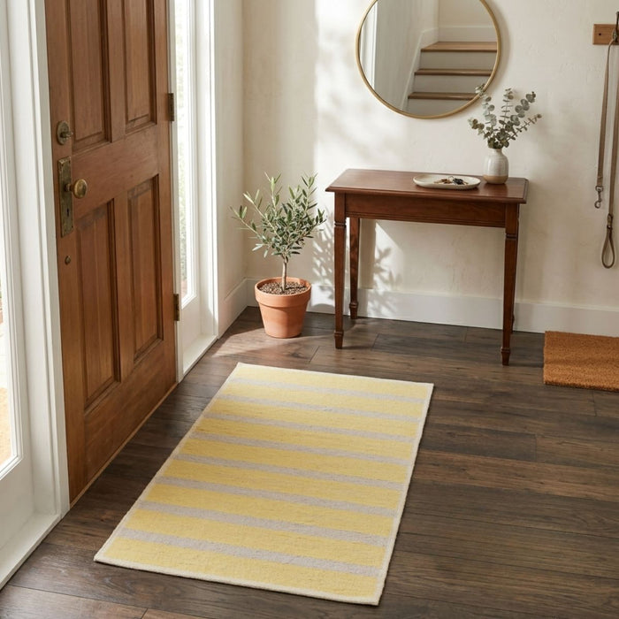 Yellow striped rug on a wooden floor in a room with a wooden door and table.